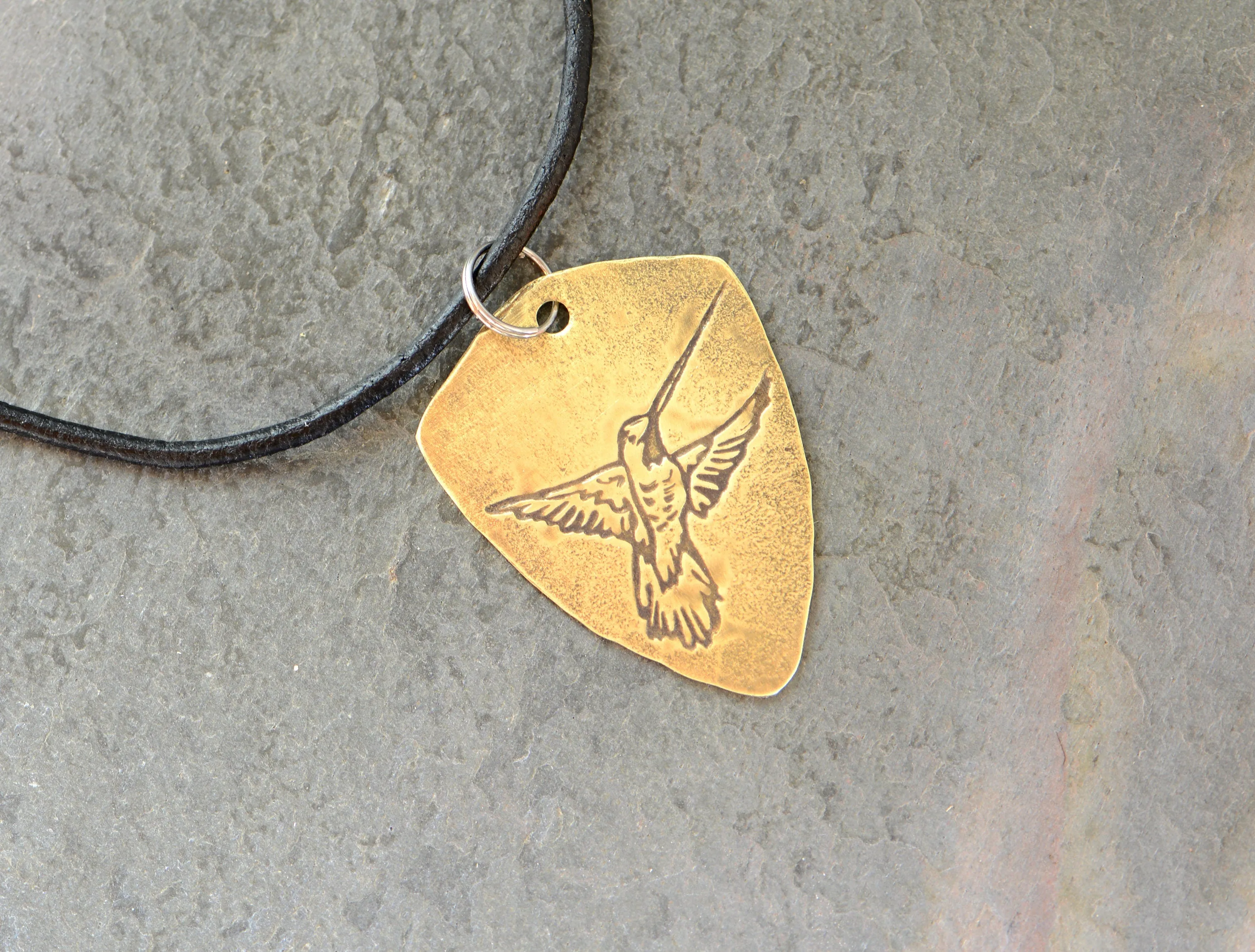 Brass shield shaped guitar pick with hummingbird and adjustable leather cord