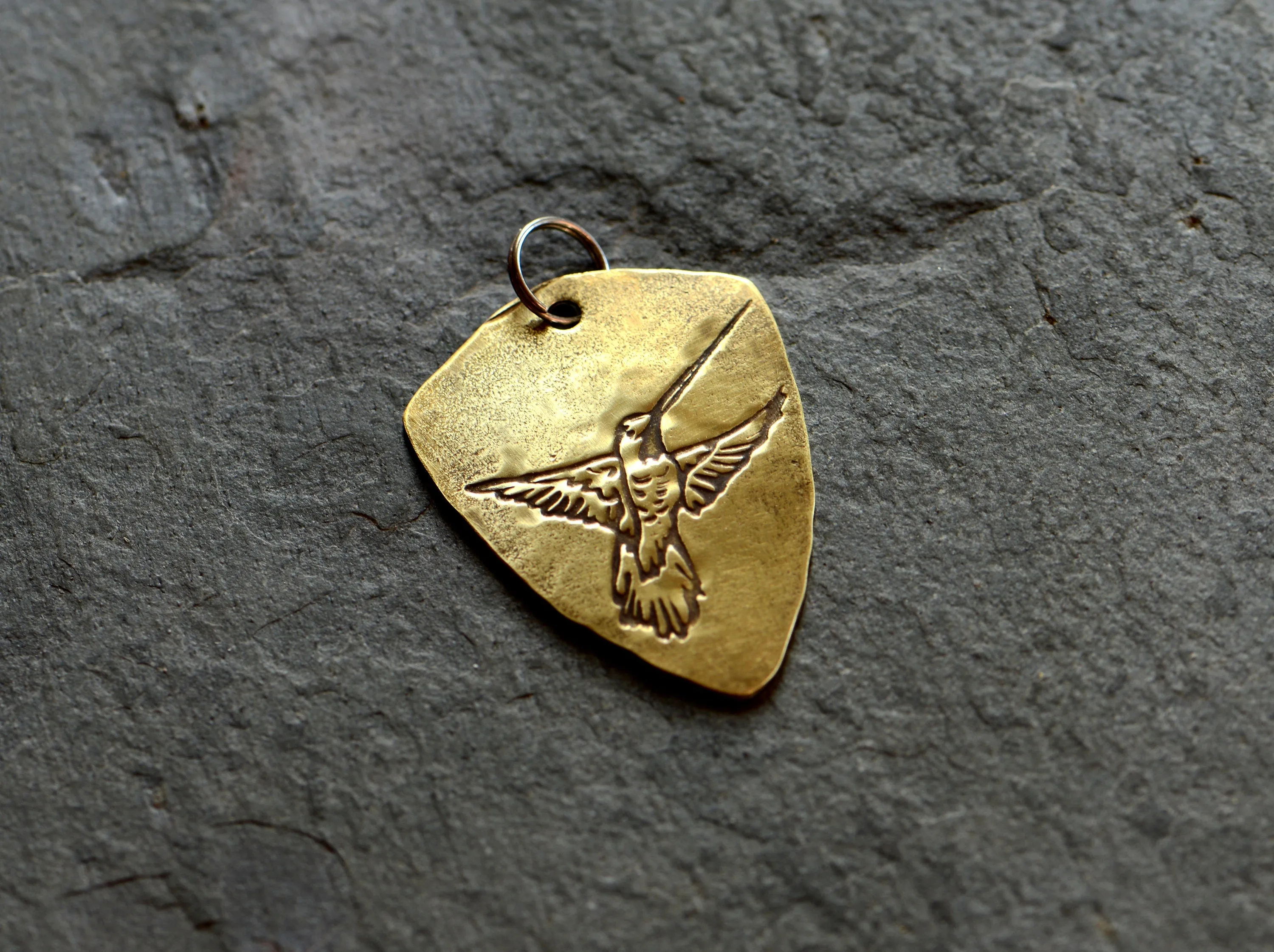 Brass shield shaped guitar pick with hummingbird and adjustable leather cord