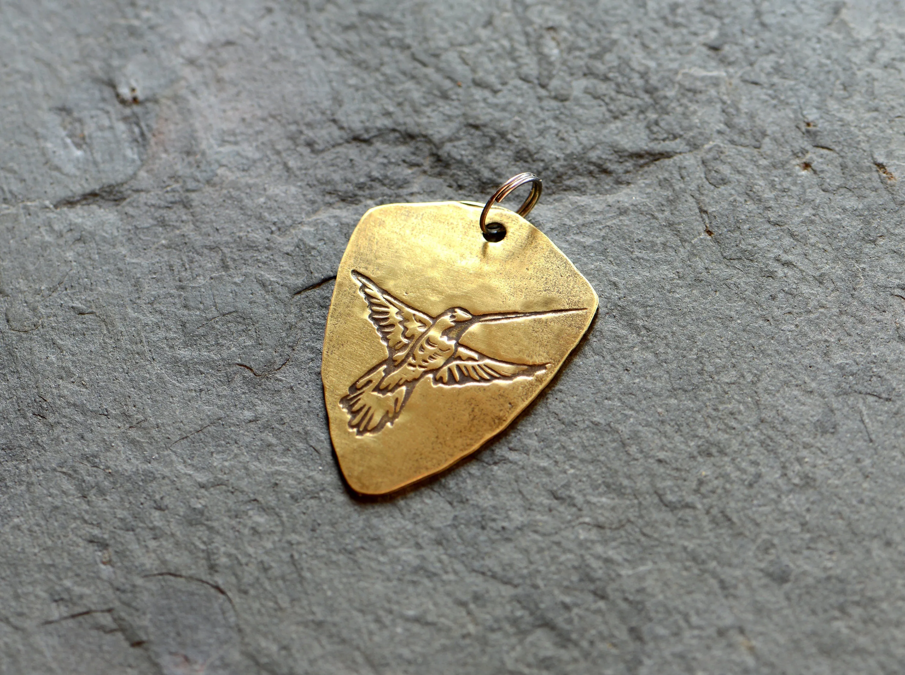 Brass shield shaped guitar pick with hummingbird and adjustable leather cord